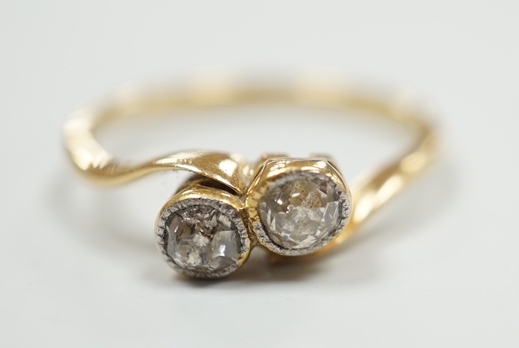 A yellow metal and collet set two stone diamond cross over ring, size L, gross weight 1.9 grams.